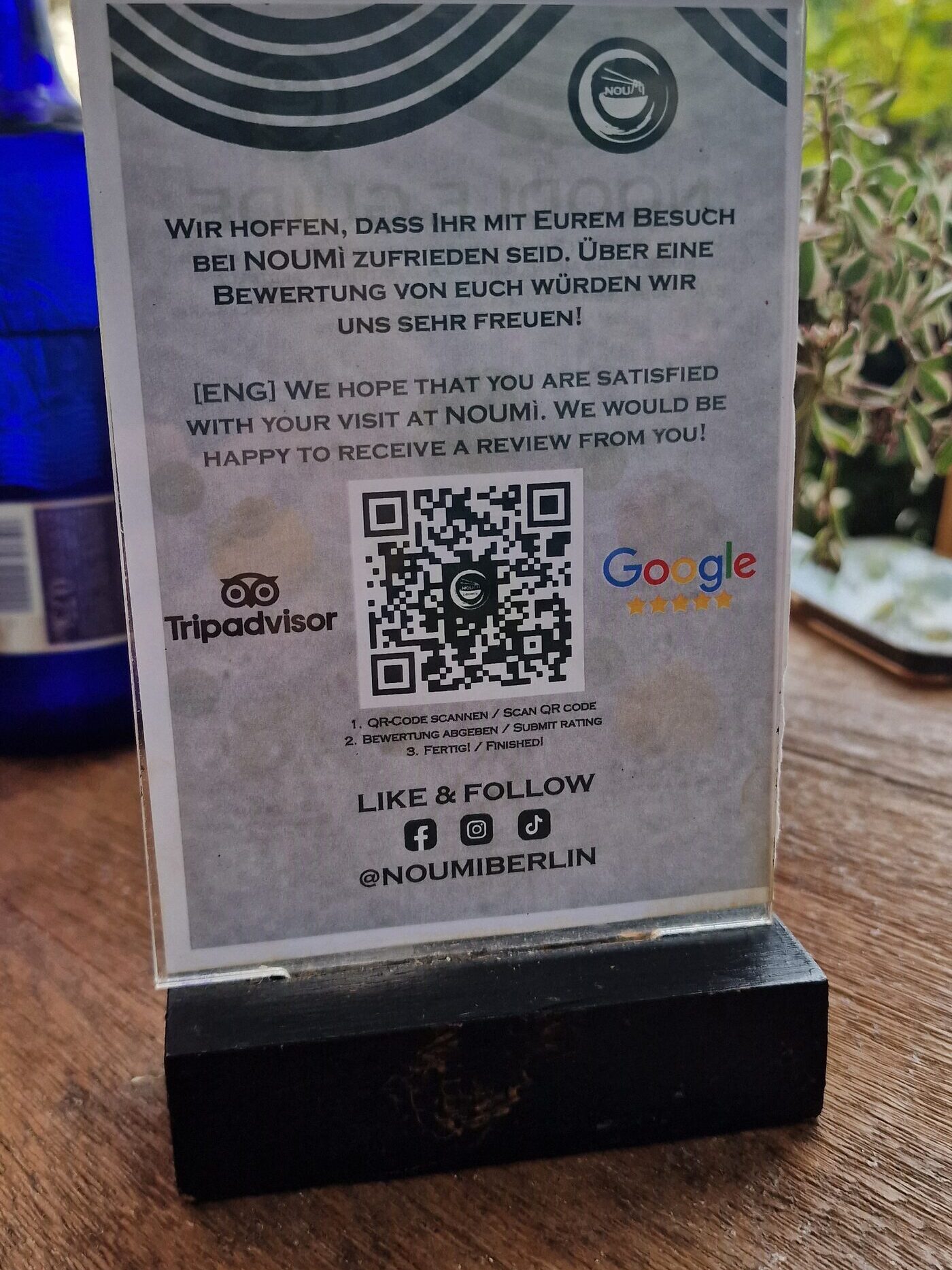 Tischaufsteller eines Restaurants: freundlicher zweisprachiger Text, QR-Code mit Schritt-für-Schritt-Anleitung, dazu Tripadvisor-, Google- und Social-Media-Logos