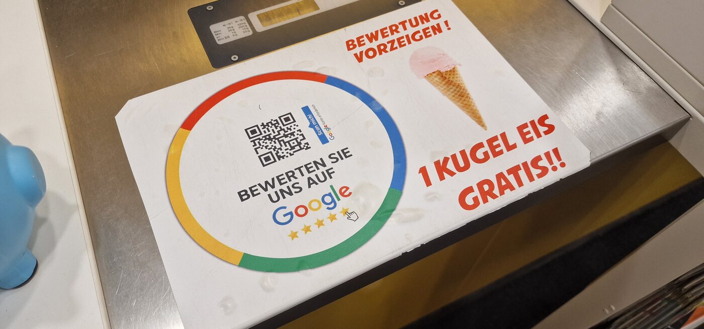 Aushang an einer Ladentheke: „Bewertung vorzeigen – 1 Kugel Eis gratis“ neben einem Google-Bewertungs-QR-Code