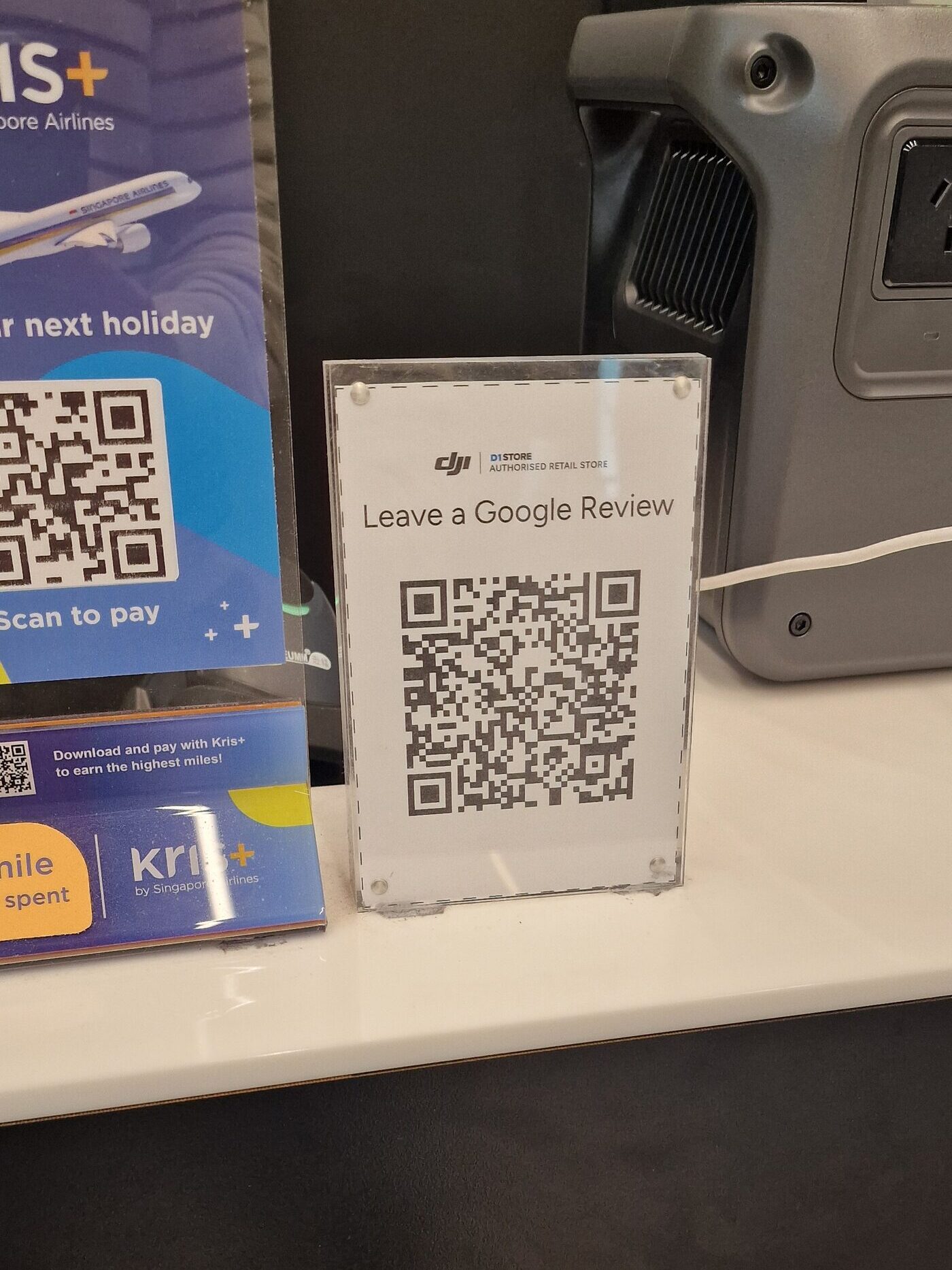 Aufsteller in einem Elektronikgeschäft: „Leave a Google Review“ mit großem QR-Code, ohne Begründung und ohne gut lesbaren Unternehmensnamen